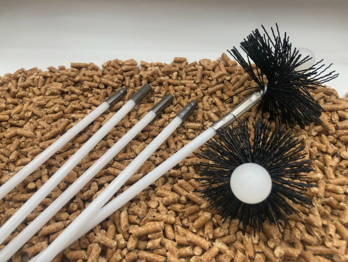 Set of five white-handled chimney cleaning rods with black bristle brushes resting on a bed of wood pellets.